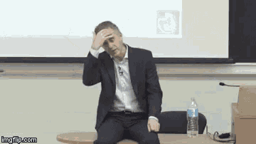 a man in a suit is sitting at a table in front of a projector screen .