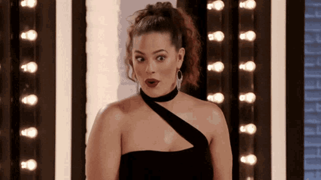 a woman in a black dress is standing in front of lights