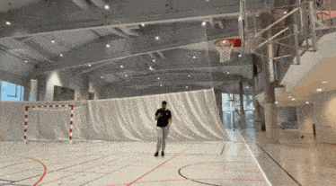 a man in a black shirt stands on a basketball court looking at his phone