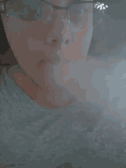 a close up of a person wearing glasses blowing smoke out of their mouth .