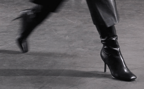 a woman wearing a pair of black boots is walking on a concrete floor