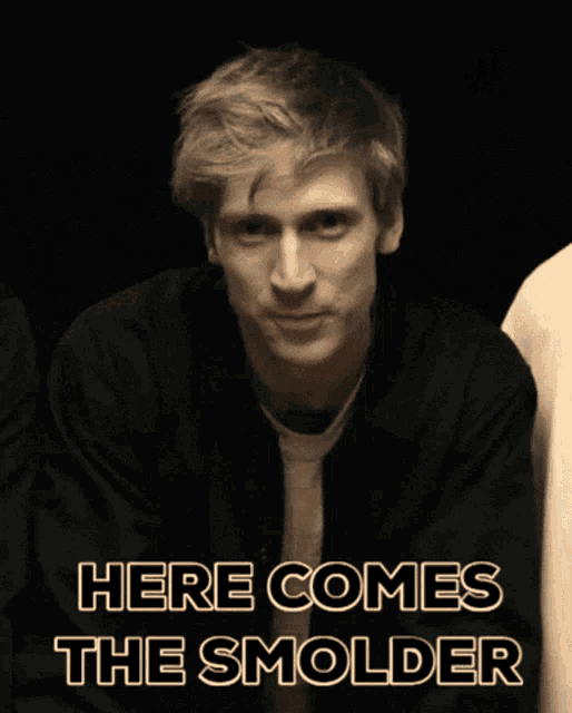 a man in a black jacket with the words here comes the smolder behind him