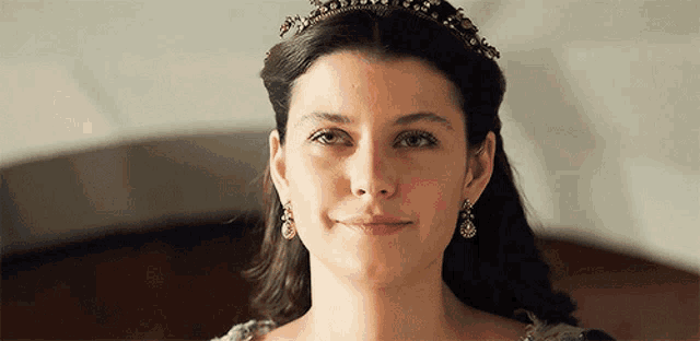 a woman wearing a tiara and earrings smiles
