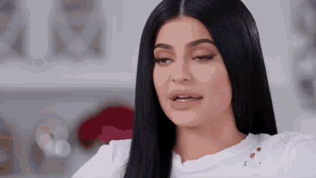 a woman with long black hair and a white shirt is making a funny face .