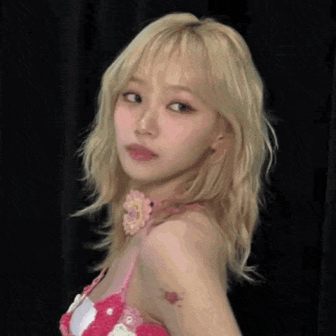 a woman with blonde hair and a tattoo on her arm is wearing a pink top and looking at the camera .