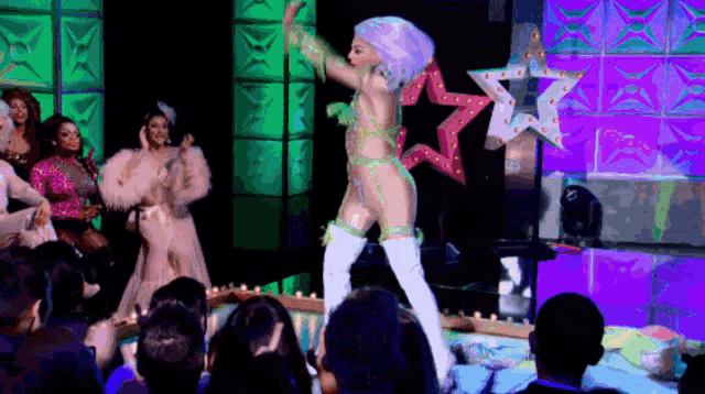a drag queen is performing on stage in front of a crowd of people .