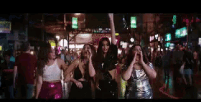 a group of young women are dancing in a crowded street at night .
