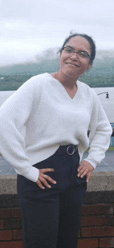 a woman wearing a white sweater and black pants stands with her hands on her hips