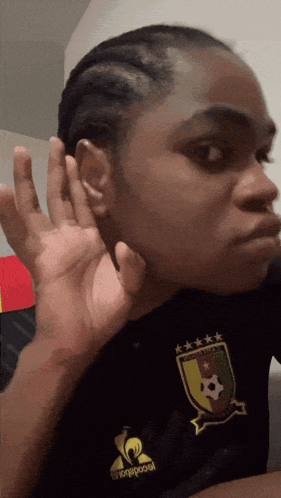 a woman wearing a black shirt that says le coq sportif holds her hand to her ear