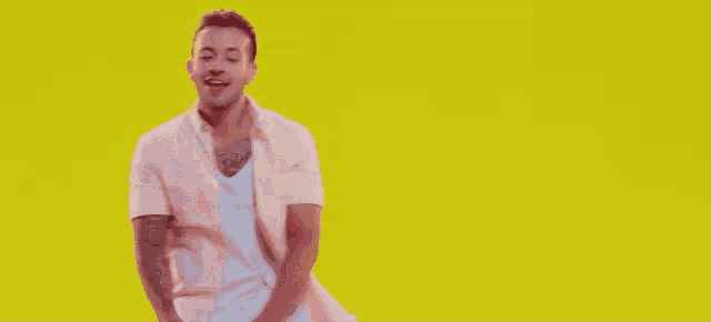 a man in a pink shirt and white tank top is dancing on a yellow background
