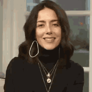 a woman wearing a black turtleneck , earrings , and necklaces is smiling .