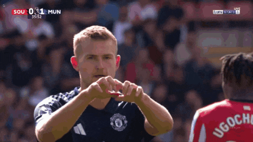 a soccer player making a heart with his hands in front of another player