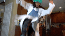a person in a lab coat and green hat is jumping in the air in a kitchen .