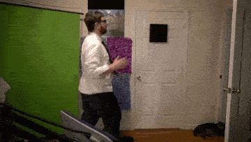 a man in a white shirt and tie is standing in front of a green screen in a room .