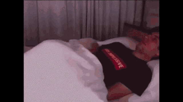 a man is laying in bed wearing a black supreme shirt .