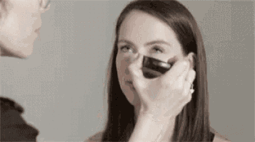 a woman is getting her makeup done by a woman .