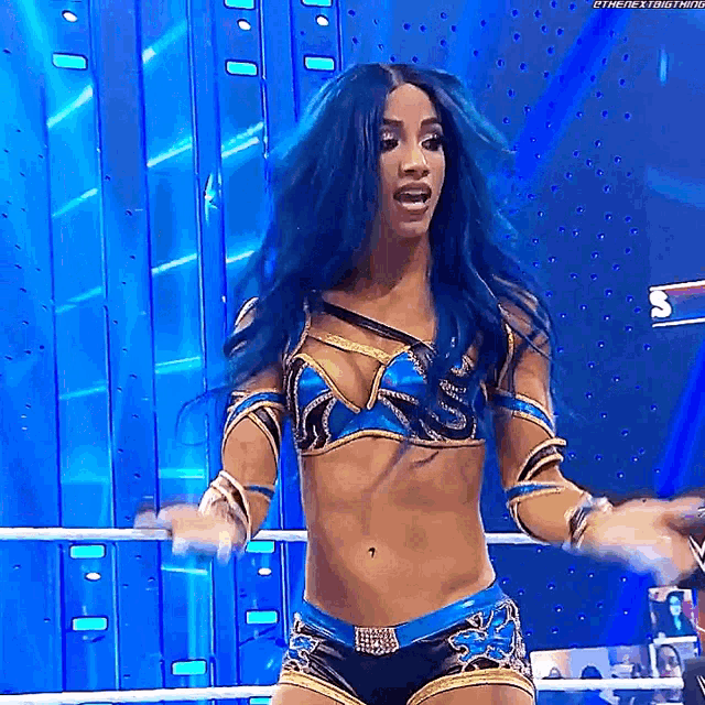 a woman with blue hair is standing in a wrestling ring with her hands in the air .