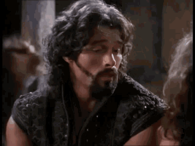 a man with a beard and curly hair is wearing a black vest .