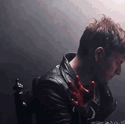 a man in a leather jacket is sitting in a chair with his hands in blood .