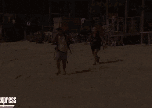 a man and a woman are running on a sandy beach with the express newspaper behind them