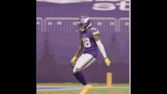 a football player in a purple uniform is jumping in the air while holding a football .