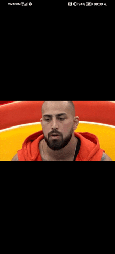 a man with a beard wearing a red hoodie is looking at the camera .