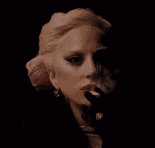 lady gaga is smoking a cigarette in a dark room .