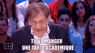 a man in a suit is sitting in front of a crowd and saying tu va manger une tarte academice