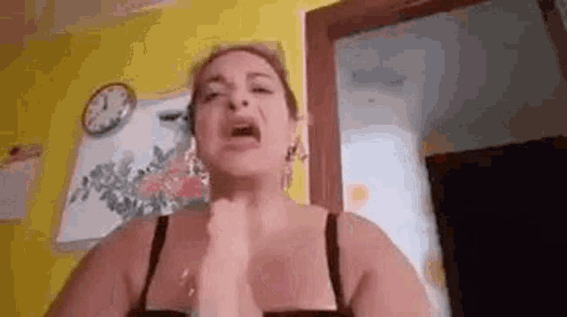 a woman in a black bra is making a funny face in front of a yellow wall and a clock .