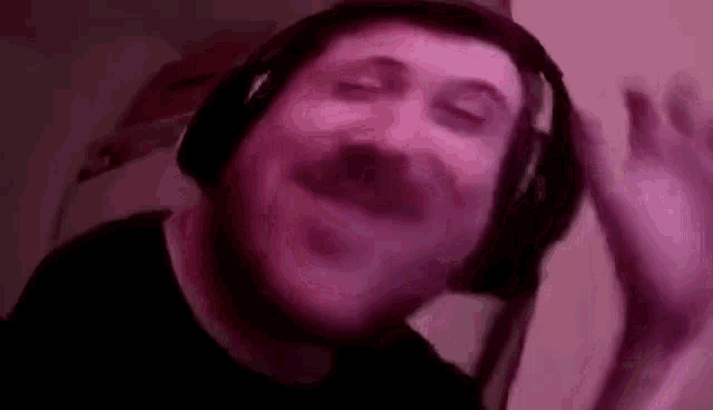 a man with a mustache is wearing headphones and waving his hand .