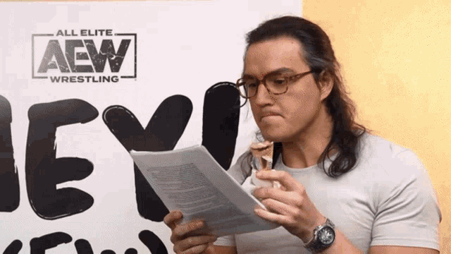 a man eating a sandwich in front of a sign that says aew