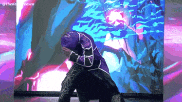 a man in a purple jacket is kneeling down in front of a purple and blue background .