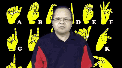 a man wearing glasses stands in front of a sign language alphabet including a b c d e f and k