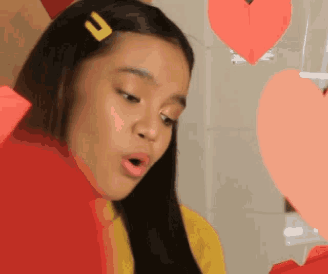 a young girl with a yellow clip in her hair is surrounded by paper hearts .