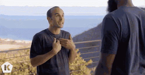 two men are standing next to each other on a balcony and one of them is talking to the other .