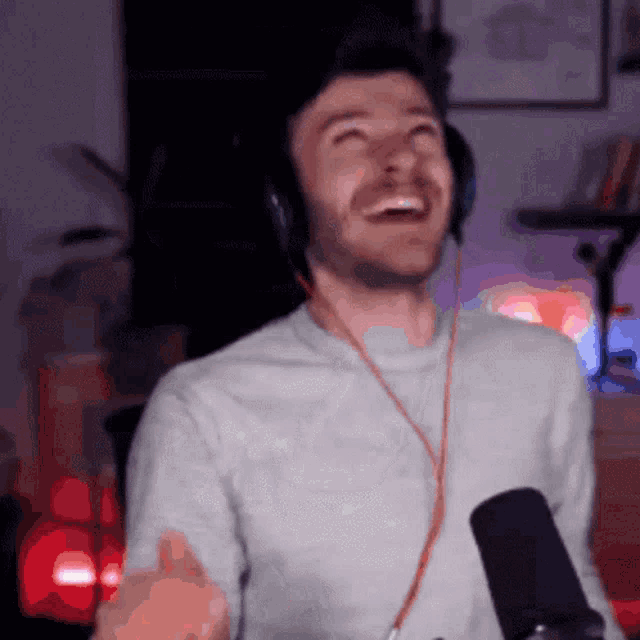 a man wearing headphones and a gray shirt is laughing in front of a microphone .