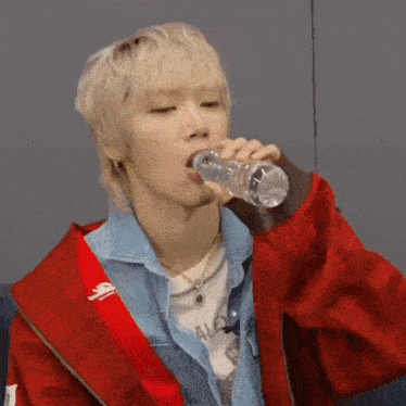 a man in a red jacket is drinking water from a plastic bottle .