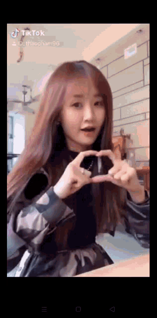 a woman making a heart shape with her hands on a tiktok video