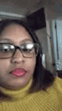 a woman wearing glasses and a yellow sweater is looking at the camera .