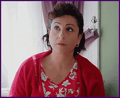 a woman wearing a red cardigan and a floral shirt looks at the camera