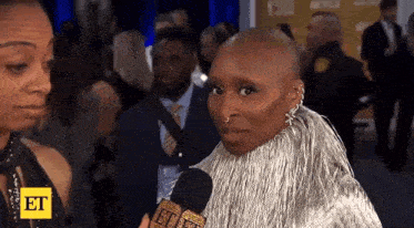 a woman with a shaved head is talking into a microphone while standing on a red carpet .