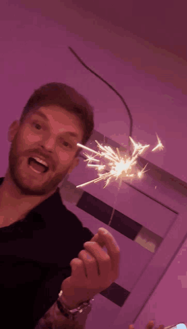 a man with a beard is holding a sparkler in front of his face