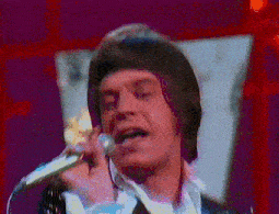 a man singing into a microphone in front of a red curtain