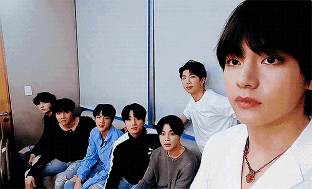 a group of young men are sitting next to each other and one of them is wearing a necklace