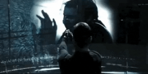 a man is looking at his reflection in a mirror while a woman looks on .