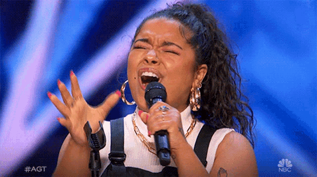 a woman is singing into a microphone with her mouth open on a stage .
