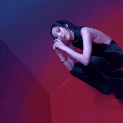 a woman in a black dress is squatting down in a red room