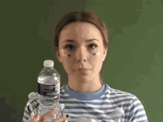 a woman in a striped shirt is holding a bottle of water in front of her face .