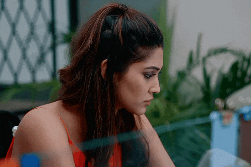 a woman in a red tank top is sitting at a table looking down