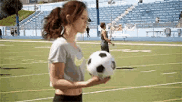 a woman is holding a soccer ball in her hand on a soccer field .